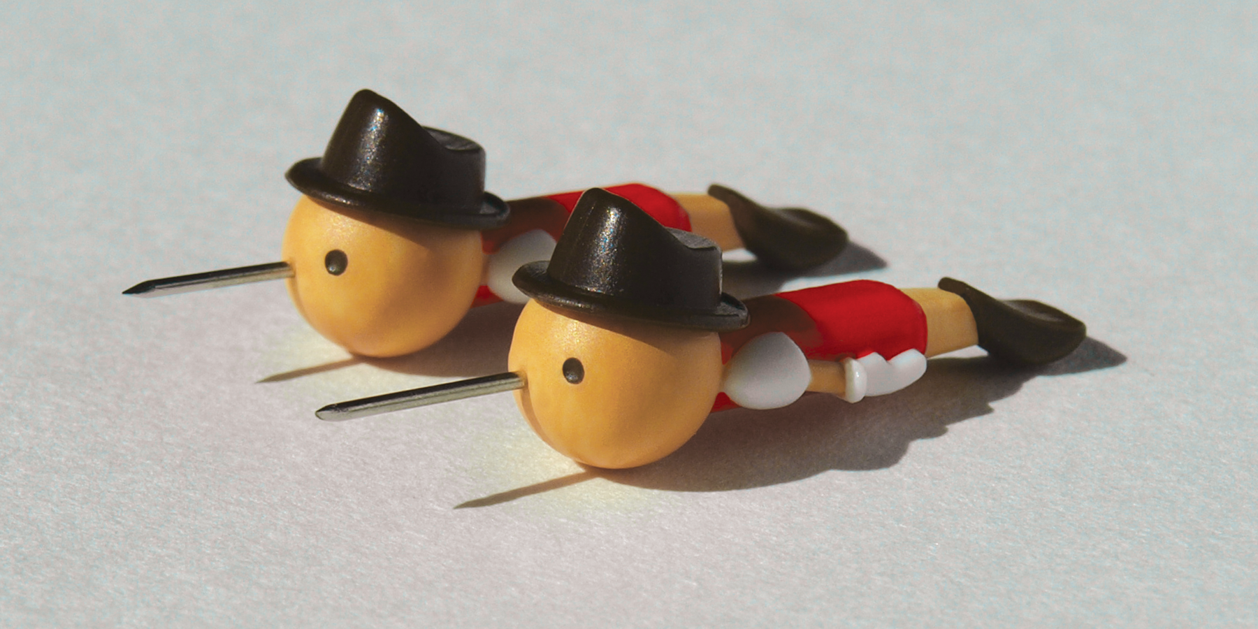Two real boy push pins lying side by side on a grey surface