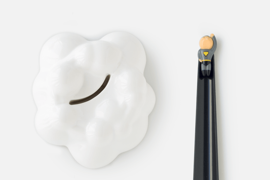 Shoeperhero (Black) laid flat next to the ceramic cloud stand that keeps it upright when not in use