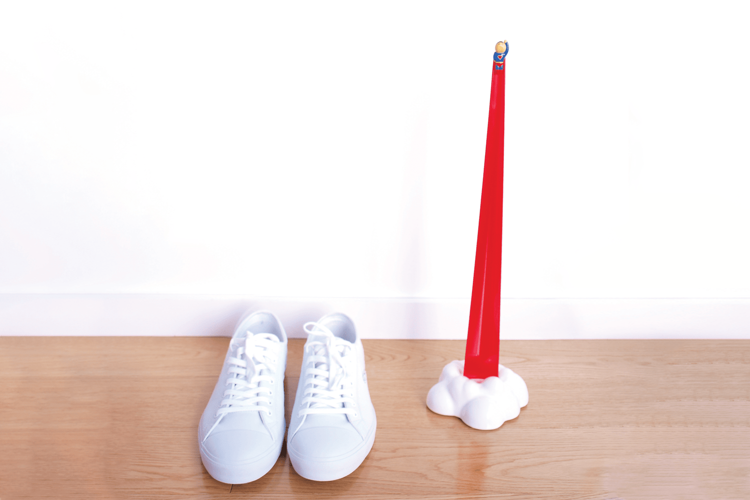 Red Shoeperhero shoehorn in it's cloud stand positioned next to a pair of white shoes