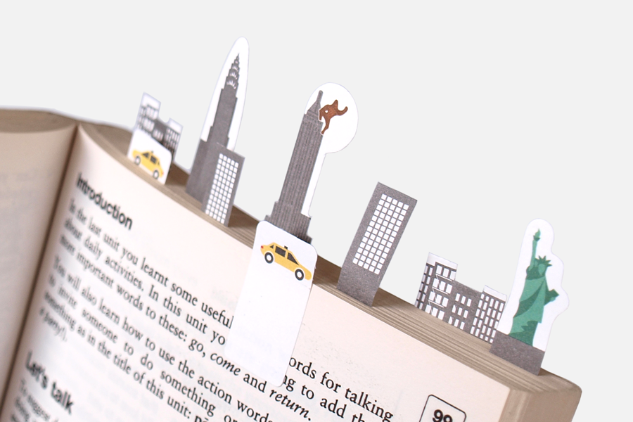 Book filled with paper tabs representing iconing features of New York city skyline on light grey background