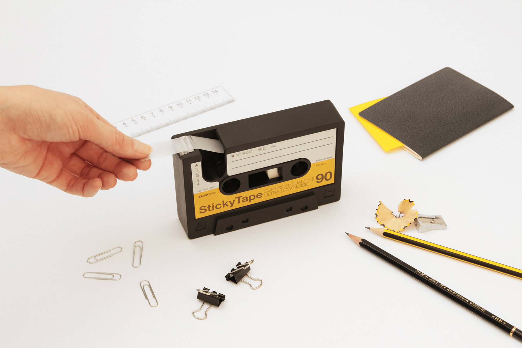 tape cassette dispenser with hand removing a section of tape. Surrounded by other stationery design items including pencils andf notepads