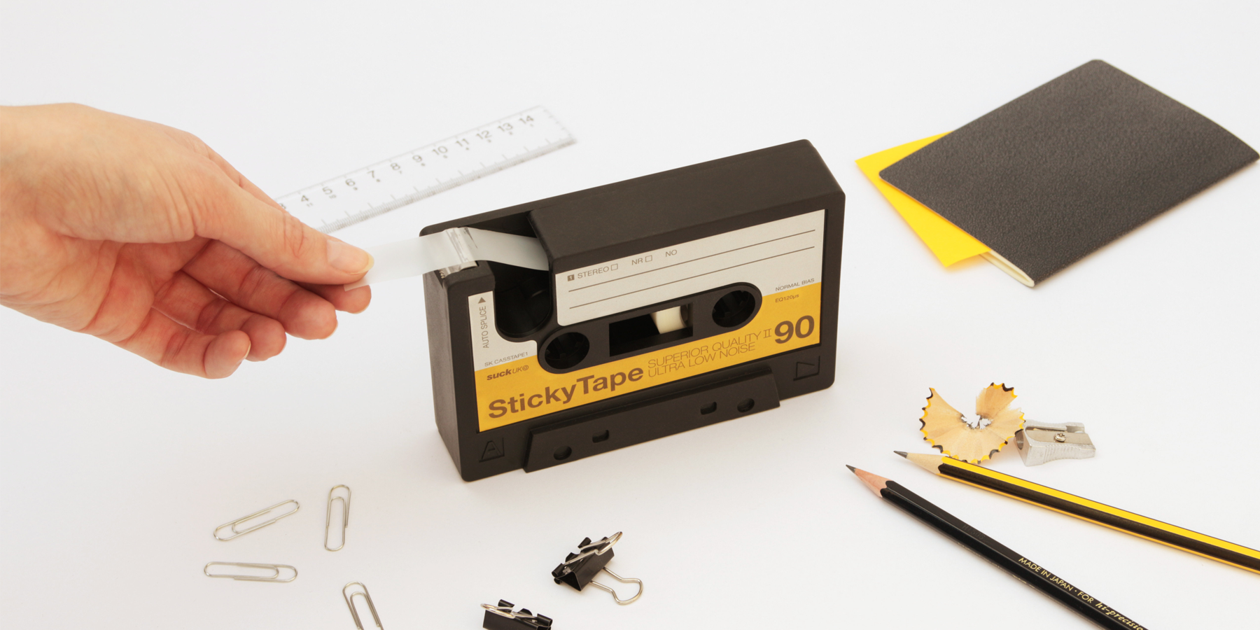 tape cassette dispenser with hand removing a section of tape. Surrounded by other stationery design items
