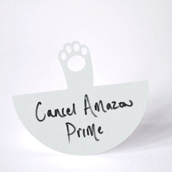 paper grey cat paw rocking from side to side in a waving action on it's arced base, with the example note "Cancel Amazon Prime" written on it as a reminder