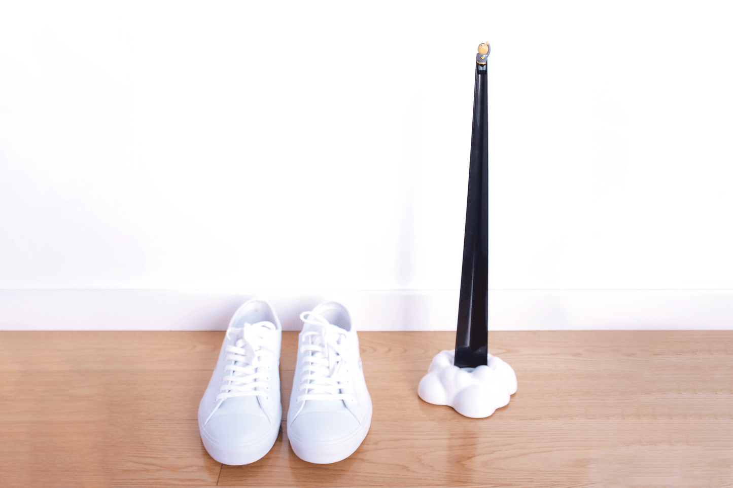 Black Shoeperhero shoehorn in it's cloud base, next to a pair of white shoes in a japanese interior